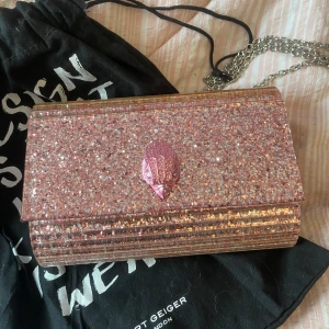 Glittrig rosa kuvertväska från Kurt Geiger - Snygg glittrig rosa väska från Kurt Geiger.  Har använt den några gånger men den är i nyskick därför säljer jag den för 800kr då den kostade 1545kr då jag köpte den. Fin färg till sommaren! ✨