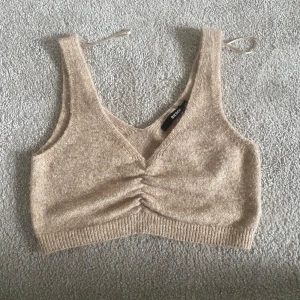 Beige stickad topp från Bikbok  - Säljer en beige stickad topp från Bikbok. Toppen har en v-ringad design med ribbade kanter och en snygg rynkad detalj framtill. Perfekt för en stilren och bekväm look. Säljer då den inte kommer till användning längre. Den är i bra skick men lite nopprig. Skriv för fler bilder eller frågor!💕