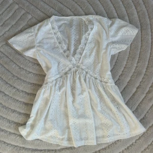 Vit blus med spetsdetaljer - Vit blus med v-ringning och spetsdetaljer. Blusen har korta ärmar och ett broderat mönster. Aldrig använd🤍