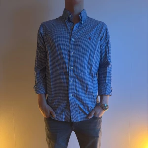 Ralph Lauren Blå och vit rutig skjorta - Snygg blå och vit rutig skjorta med knappar och långärmad design. Perfekt för en stilren look. Skjortan har en klassisk krage och är tillverkad i ett bekvämt material.