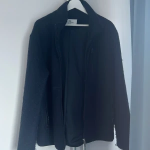 Mörkblå jacka från John Henric - Säljer en stilren svart jacka från John Henric. Jackan har en dragkedja framtill och är långärmad. Perfekt för kyligare dagar med sitt mjuka material.