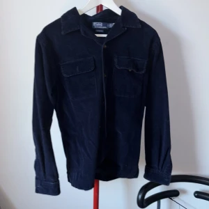Mörkblå manchester overshirt från Polo Ralph Lauren - Snygg mörkblå overshirt i manchester från Polo Ralph Lauren. Skjortan har långa ärmar och två bröstfickor med knappar. Perfekt för en stilren och avslappnad look. Priset kan diskuteras!