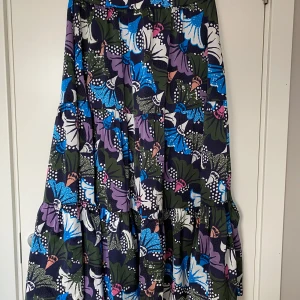 Mönstrad långkjol från Carin Wester - Säljer en färgglad långkjol från Carin Wester i storlek 44. Kjolen har ett livfullt blommönster i blått, lila, grönt och vitt. Tillverkad i 100% polyester, perfekt för en stilfull look. Obs! Upplever den som en stl 42 i midjan.