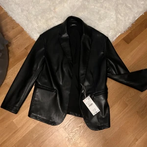 Svart skinnjacka från Zara - Snygg svart skinnjacka från Zara med klassisk design. Jackan har långa ärmar och stilrena fickor framtill. Perfekt för en trendig look.