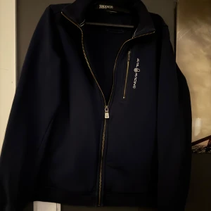 Mörkblå jacka från Sail Racing - Snygg mörkblå zip tröja från Sail Racing med dragkedja framtill och en bröstficka med dragkedja. Perfekt för en stilren look! Tröjan är i storlek S men passar även Xs