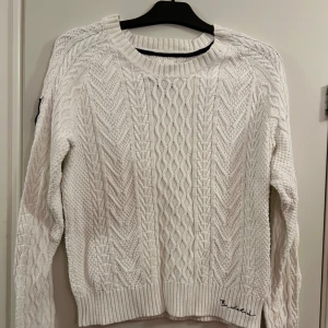 Vit stickad tröja från Bondelid - Vit stickad tröja från Bondelid med ett klassiskt kabelstickat mönster. Tröjan har en broderad logga på ärmen samt vid nederkanten. Använd några gånger men i mycket bra skick. Ordinariepris är 699. 
