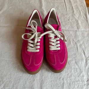 Rosa custommade sneakers med snörning - Snygga rosa sneakers custommade med vit snörning och brun sula. Skorna har en sportig design med kontrasterande vita detaljer och en bekväm passform. Perfekta för en färgglad stil.