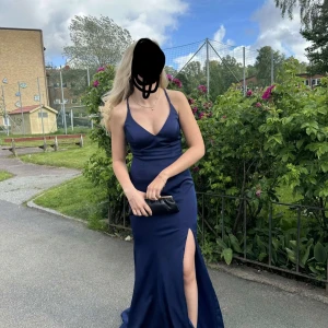  balklänning med slits - Elegant mörkblå långklänning med smala axelband och djup v-ringning. Klänningen har en hög slits och en öppen rygg med korsade band. Perfekt för en speciell kväll! eftersom det är snörning i ryggen kan man anpassa storleken