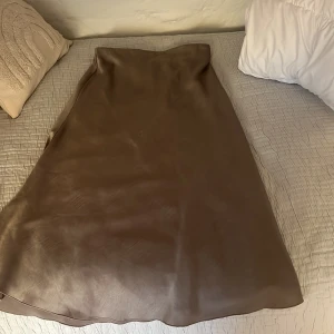 Brun långkjol från Weekday - Snygg brun långkjol från Weekday i ett stilrent och enkelt snitt. Kjolen har en mjuk och slät yta som ger en elegant look. Perfekt för att matcha med olika toppar. 