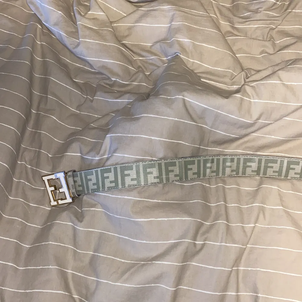 Snyggt grått bälte från Fendi med det ikoniska FF-mönstret. Bältet har ett stort guldfärgat spänne med Fendi-logotypen. Perfekt för att ge en lyxig touch till din outfit. Den har skador vid hålen men går säkert att laga själv, gjorde extra hål så det passar 100-125. Muu.
