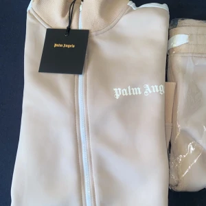 Beige Palm Angels dress (Helt Ny) - En stilren Palm Angels dress i beige färg, storlek S. Den har en modern och avslappnad passform, perfekt för både vardag och fest. Materialet är högkvalitativt, den är dessutom mjuk och bekväm. OBS! (Pris kan diskuteras vid intresse)