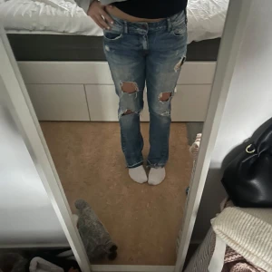 Blå jeans med slitningar - Snygga blå jeans från Zara men köpta här på plik med slitningar på knäna och nitar längs linningen. 39cm i midjemått💕