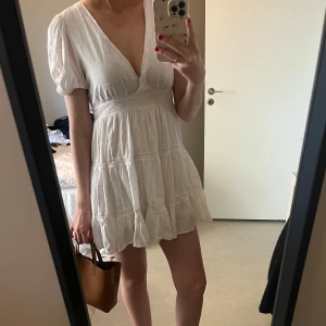 Vit kortklänning med v-ringning - Säljer en söt vit kortklänning med v-ringning och puffiga kortärmar från Zara. Klänningen har en smickrande passform med volangdetaljer och spetsinslag som ger en gullig touch. Perfekt för sommarens alla tillfällen!