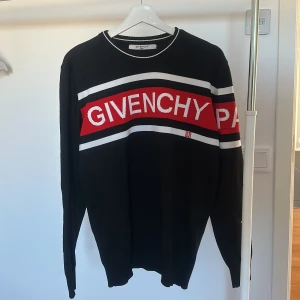 Svart tröja från Givenchy - Snygg svart tröja från Givenchy med röd och vit text på bröstet. Tröjan har långa ärmar och en rund halsringning med vita detaljer. Perfekt för en stilren look.  Mycket fint tyg. Fick den i present för några år sedan. Finns inget som tyder på storlek men skulle säga mellan m/xl.