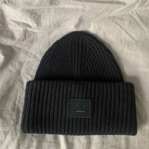 SÖKER Svart ribbad mössa med broderad detalj - Snygg svart ribbad mössa med en broderad detalj framtill. Perfekt för att hålla värmen under kyliga dagar. Stilren och enkel design som passar till det mesta.