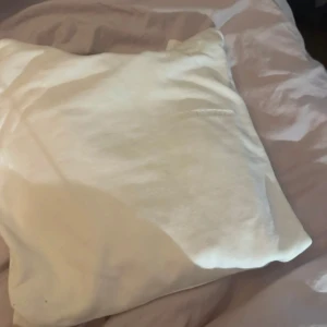 Vit hoodie från J.Lindeberg - Säljer en stilren vit hoodie från J.Lindeberg. Tröjan har en diskret logga på bröstet och tryckknappar vid kragen. Perfekt för en minimalistisk look.