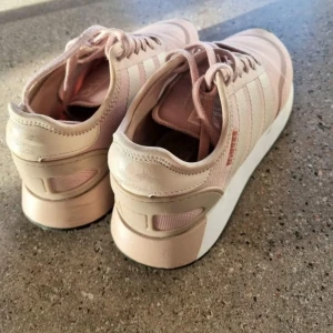 Rosa sneakers från Adidas - Snygga rosa sneakers från Adidas med klassiska ränder på sidan. Skorna har en bekväm sula och snörning framtill. Perfekta för en avslappnad stil.