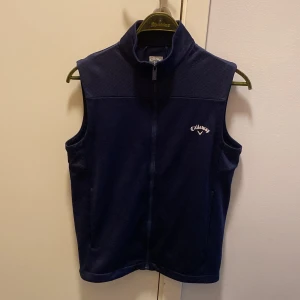 Mörkblå fleeceväst från Callaway - Säljer en mörkblå fleeceväst från Callaway. Västen har en dragkedja framtill och en broderad logotyp på bröstet. Perfekt för kyligare dagar när du behöver lite extra värme.
