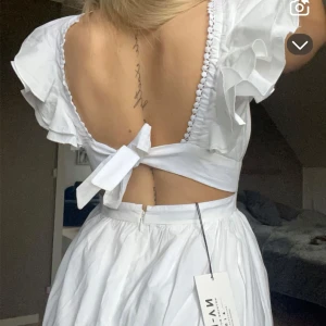 Vit klänning från NA-KD - Säljer en söt vit klänning från NA-KD med volangdetaljer och öppen rygg. Klänningen har en v-ringad design och knytning i ryggen. Perfekt för sommarens eller student 🤍🌸 aldrig använd med prislapp kvar, säljer så jag hittat en annan studentklänning