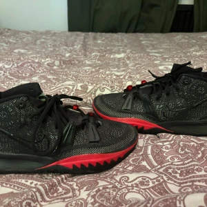Kyrie 7 (Basketskor) - KOM MED PRIS, NY PRIS 3500kr                                                       Snygga svarta Nike sneakers med röda detaljer och snörning. Skorna har en robust sula med mönster och en röd Nike-logga på sidan. Perfekta för en sportig look.