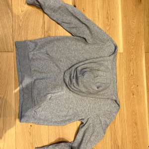 Grå hoodie - Säljer en stilren grå hoodie i mjukt material. Perfekt för en avslappnad look. Den har en klassisk design med huva och långa ärmar. Slim fit 