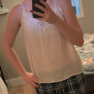 Beige linnetopp från Rut & Circle - Säljer en stilren beige linnetopp från Rut & Circle med spetsdetaljer vid halsringningen. Toppen har tunna axelband och en mjuk, lätt känsla. Perfekt för varma dagar eller som ett lager under en kavaj. Den är även lite see through