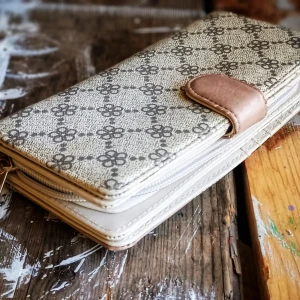Mönstrad plånbok från Dudlin Accessories - Snygg plånbok med ett unikt mönster i beige och grått. Den har flera fack för kort och en dragkedja för mynt. Designen är kompletterad med detaljer i rött och svart samt en elegant knappstängning.