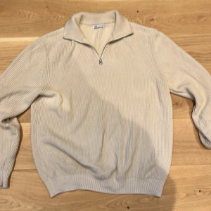 Beige ribbad tröja med dragkedja - Säljer en stilren beige tröja från Gant med ribbad struktur och dragkedja vid halsen. Perfekt för en avslappnad men ändå snygg look. Tröjan har långa ärmar och en klassisk passform.