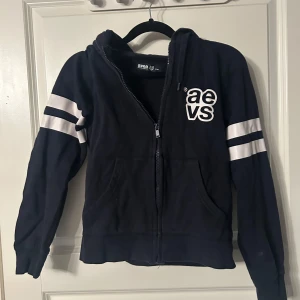 Marinblå hoodie från Svea - Säljer en Marinblå hoodie från Svea med vita ränder på ärmarna. Tröjan har dragkedja och långa ärmar, perfekt för en avslappnad stil. Hör av dig vid intresse!