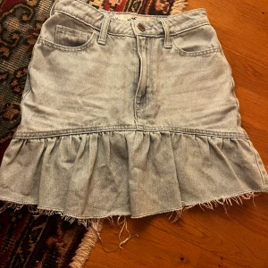 Jeanskjol från Hollister - Säljer en snygg jeanskjol från Hollister i ljusblå denim. Kjolen har en volangdetalj och fransad nederkant som ger en cool look. Den är ultra high-rise men jag själv brukar ha lång tröja över. Säljer då den har blivit för liten💕