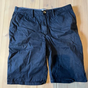 Mörk blå shorts från RYVLS - Snygga mörk blå shorts från RYVLS i en klassisk design. De har en knapp och dragkedja framtill samt praktiska fickor både fram och bak. Perfekta för både golfbana eller bara vara på stranden