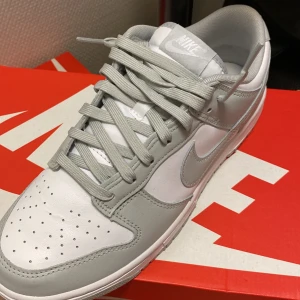 Nike Dunk Low Retro i vit och grå - Snygga Nike Dunk Low Retro sneakers i en stilren vit och grå färgkombination. Grey fog. Väldigt eftertraktade. Nypris 1500kr oanvända, helt nya