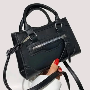 Svart handväska med dragkedja - Snygg svart handväska i skinn med praktisk dragkedja framtill. Perfekt för att bära dina nödvändigheter med stil. 