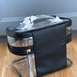 Transparent necessär med svarta detaljer - Säljer en superpraktisk och stilren transparent necessär väska frå Victoria’s secret med svarta detaljer. Perfekt för att hålla ordning på dina saker när du reser eller bara för att ha hemma. Den har en dragkedja i guld och ett handtag på toppen. Väldigt lätt att rengöra och ser riktigt snygg ut!