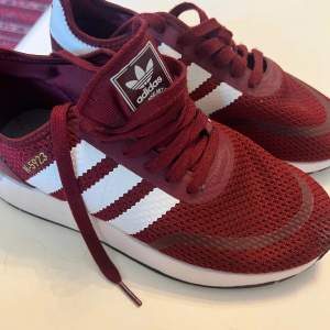 Säljer ett par snygga burgundy Adidas sneakers i storlek 38, (N-5923 original). Skorna har en klassisk design med vita ränder och är tillverkade i ett andningsbart syntetmaterial. Perfekta för både vardag och träning!  ord pris 1000kr+