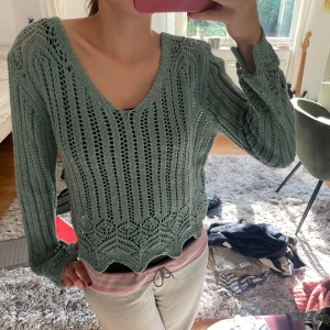Grön stickad tröja med v-ringning - Säljer en superfin grön stickad tröja med v-ringning. Den har ett snyggt hålmönster och vågig kant nertill. Perfekt för höst när man vill vara både stilren och bekväm. Tröjan är långärmad och passar perfekt till både jeans och mjukisbyxor.