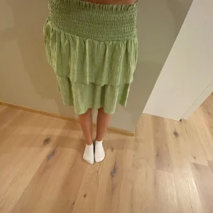 Grön volangkjol - Säljer en superfin grön kjol med volanger. Den har en elastisk midja som gör den bekväm och lätt att bära. Perfekt för sommardagar eller en avslappnad vårlook. Kjolen är i bra skick och har en härlig, luftig känsla.