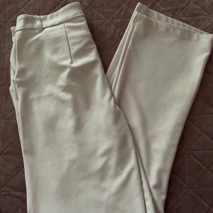 Beige byxor med knappdetalj - Säljer ett par stilrena beige byxor med knapp och dragkedja framtill. De har en klassisk look med raka ben och är perfekta för både vardag och fest. Materialet känns mjukt och bekvämt.