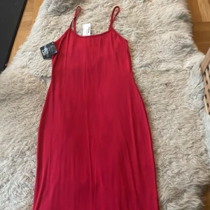 Röd klänning från NLY One Ny - Snygg röd klänning från NLY One i ett mjukt och följsamt material. Perfekt för festliga tillfällen med sin stilrena design och smala axelband. Klänningen är i nyskick och har en figurnära passform som framhäver silhuetten.