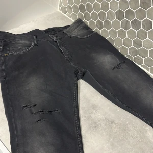 Tiger of Sweden jeans - Kag säljer ett par riktigt snygga Gråa/Svarta Tiger of Sweden jeans. Skick 9/10. Riktigt snygga jeans till bra pris med snygga slitningar! Storlek 33/32.