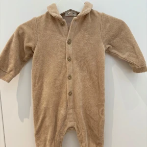 Beige/brun jumpsuit i frottématerial, storlek 56, Newbie - Beige/brun jumpsuit i frottématerial i storlek 56, Newbie. Tryckknappar i grenen för enklare blöjbyten. Använd enstaka gånger, fint skick utan anmärkningar. 