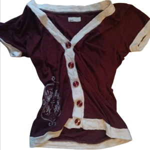  kortärmad topp med knappar - Snygg topp från Kimi med vita detaljer och knappar framtill. Den har korta ärmar och ett unikt tryck på sidan. Storlek står inte men skulle säga S