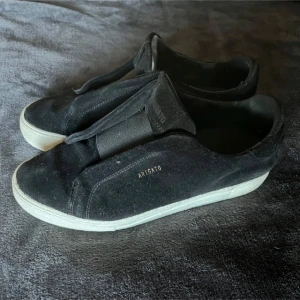 Svarta sneakers från Axel Arigato - Säljer ett par stilrena svarta sneakers från Axel Arigato i mocka. De har en vit sula och en diskret logga på sidan. Perfekta för både vardag och fest! Skorna är i bra skick och passar till det mesta i garderoben.