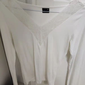 Vit långärmad topp med spetsdetaljer - Säljer en helt ny aldrig använd, superfin vit långärmad topp från Gina Tricot i storlek XS. Den har en v-ringad design med spetsdetaljer som liknar Intimissimi tröjan. Perfekt för både vardag och fest! 💫