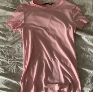Rosa t-shirt - Säljer en söt rosa t-shirt i bomull. Den är kortärmad och har en normal passform, perfekt för sommardagar eller som ett lager under en jacka. T-shirten är i bra skick och redo för en ny ägare. Passar till både vardag och festliga tillfällen!