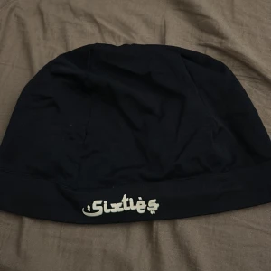 marinblå mössa från Sixties - Säljer en marinblå mössa från Sixties. Den är enkel och stilren med en broderad logga framtill. Perfekt för att hålla värmen under kyliga dagar. Passar till de flesta outfits och är ett måste i garderoben!