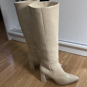 Beige stövlar med klack - Snygga beige stövlar i skinn med klack och spetsig tå, helt nya till 100%. Perfekta för höst och vinter, de har en dragkedja på sidan för enkel på- och avtagning. Stilrena och eleganta för både vardag och fest.