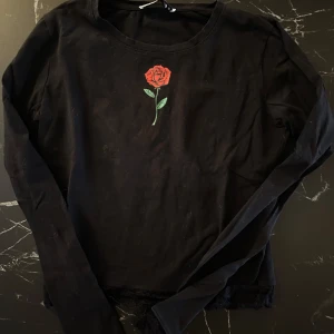 Svart långärmad tröja med rosdetalj - Säljer en svart långärmad tröja från SisterS Point med en snygg röd ros broderad på bröstet. Perfekt för höst och vår, och den är i bomull vilket gör den superbekväm. Passar både till vardags och lite finare tillfällen. 🌹