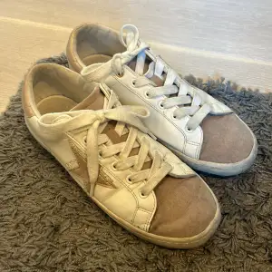 Säljer ett par vita sneakers med ljusrosa mockadetaljer och en stjärna på sidan. Skorna har snörning och är använda ganska mycket. Strl 40,5. Pris kan diskuteras!