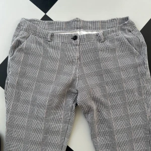 Svart-grå rutiga capribyxor - Snygga stretchiga byxor i grått och svart rutmönster. Byxorna har två fickor framtill och två fickor baktill. De har en knapp och dragkedja i midjan. Byxorna är i använt skick.  För midjemått, innerbensländ, byxlängd, se bilderna.   Storlek xl/xxl